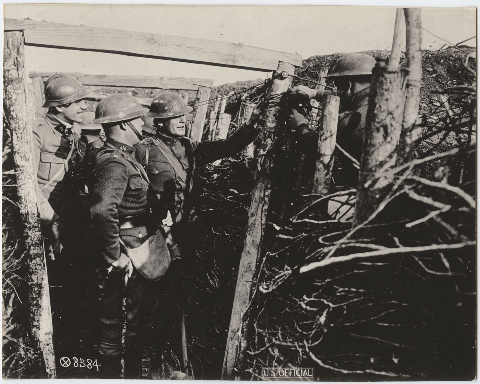 Black and white photograph. Several soldiers in uniform stand in a trench that is lined with wood supports.