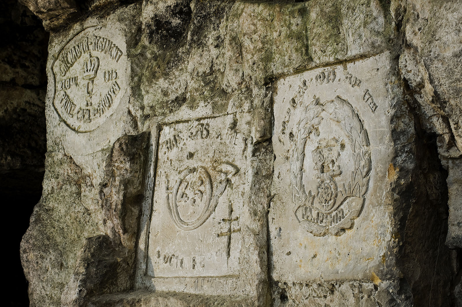 Modern photograph. Blocks of stone embedded in the wall of an underground area, carved with various words and symbols.
