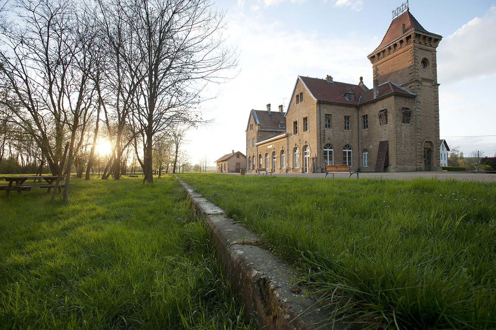 Modern photograph of a grassy area with some trees and a large stone building.