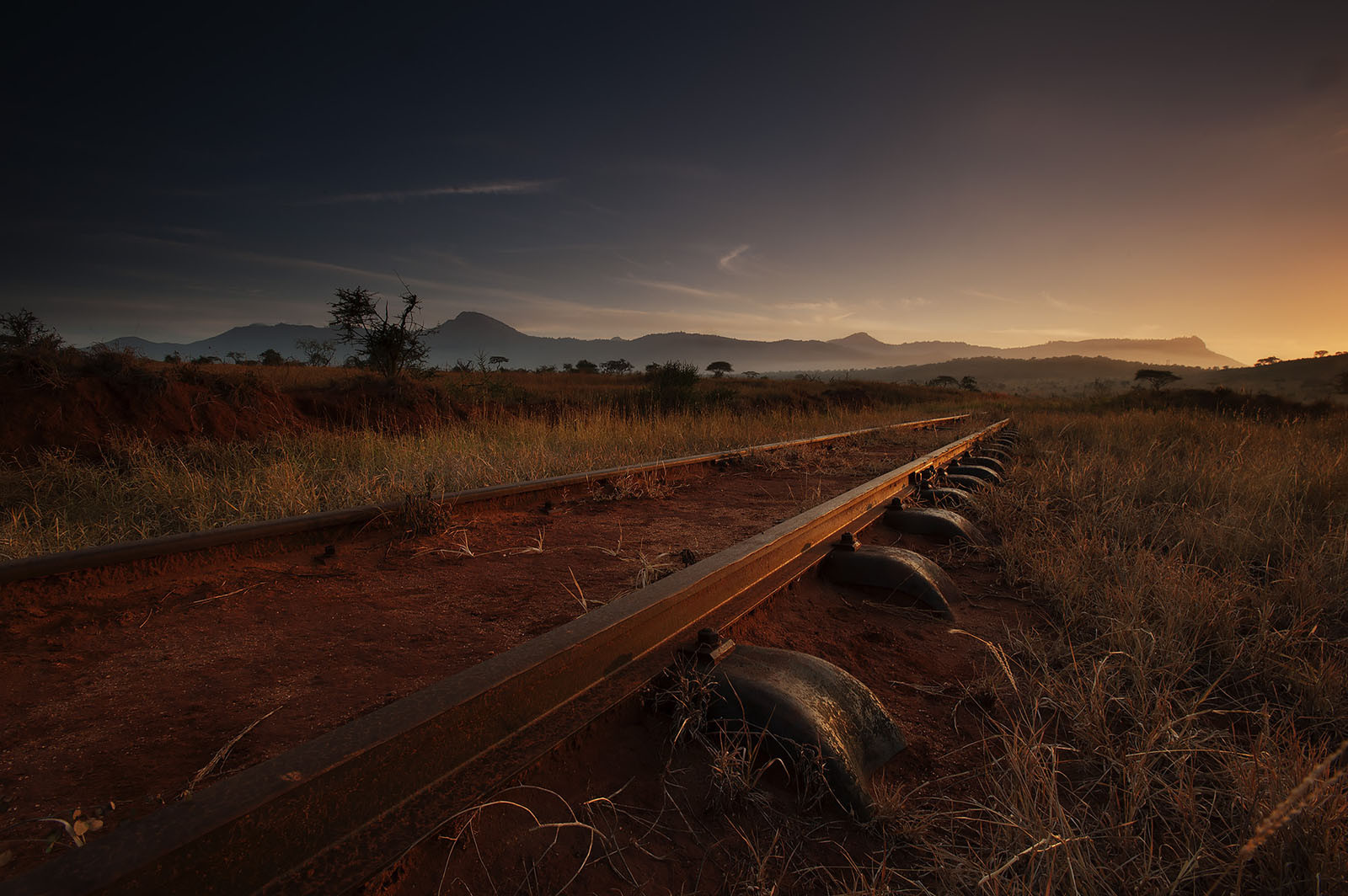 Modern photograph of a green and rust-colored grassland with railroad tracks stretching into the distance