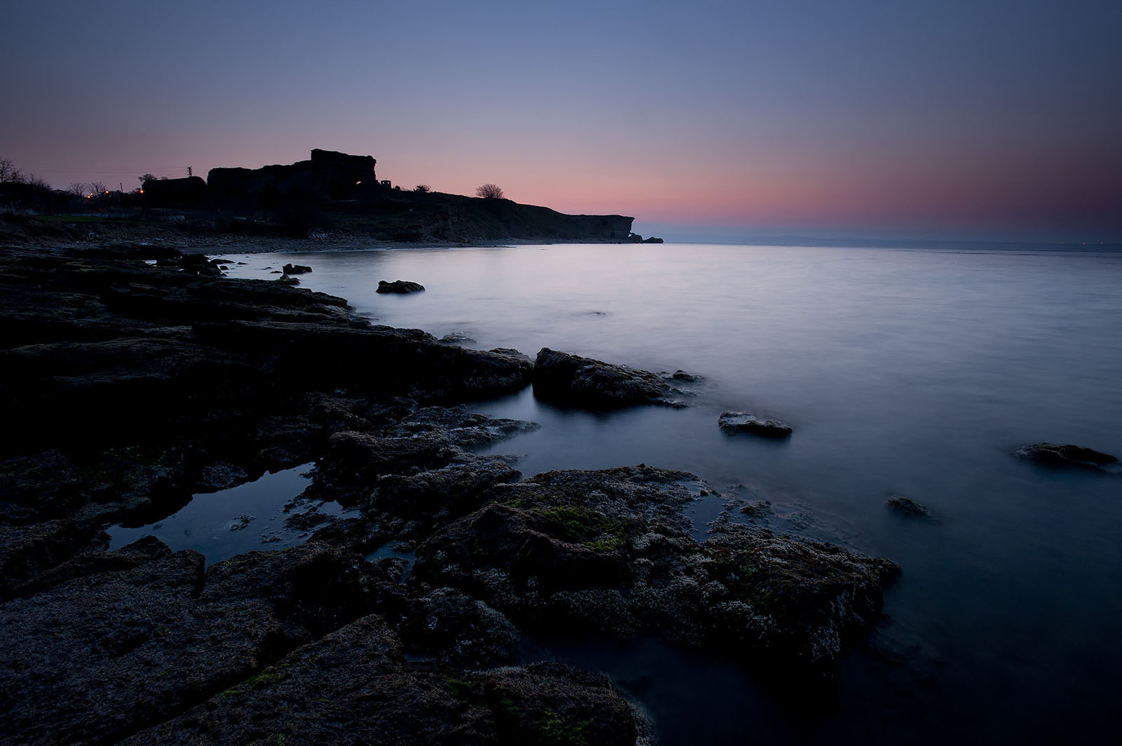 Modern photograph of a natural bay in a sea coastline, in colors of blue and orange because of sunset.