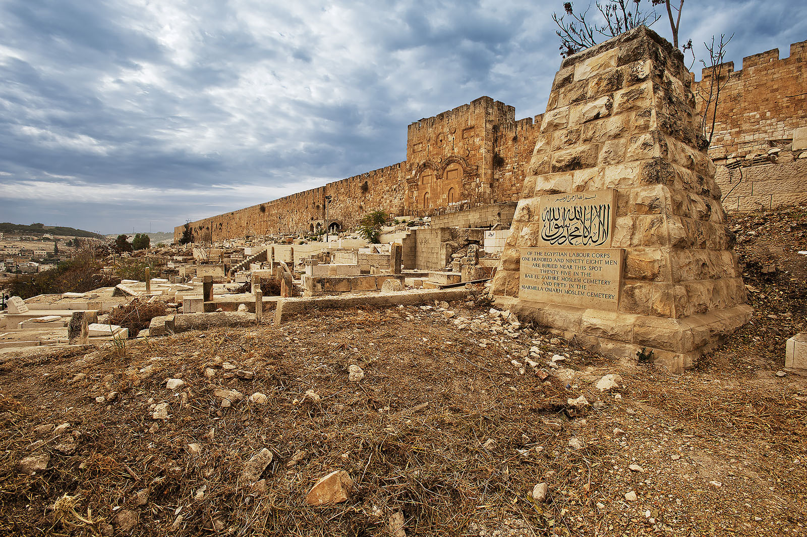 Modern photograph of a stone monument and other stone grave markers outside ancient city walls.